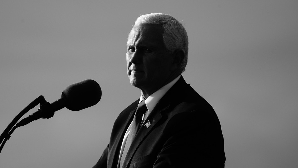 Mike Pence stands in front of a microphone, half in shadow.