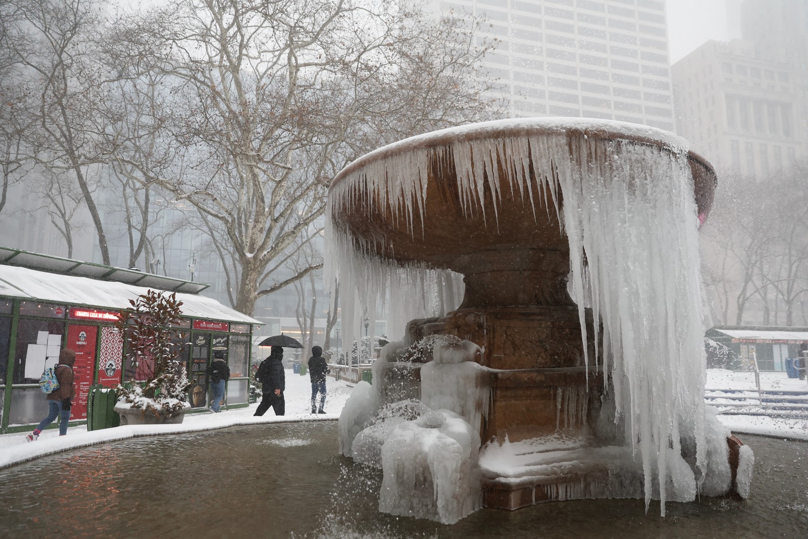 People walk around a frozen fountain in a park.