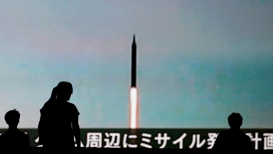 People walk in front of a monitor showing news of North Korea's fresh threat in Tokyo