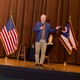 Tim Walz standing on a stage between an American flag and an Ohio flag