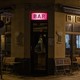 A bar at night, with an illuminated pink sign in the center and folded up tables along its windows