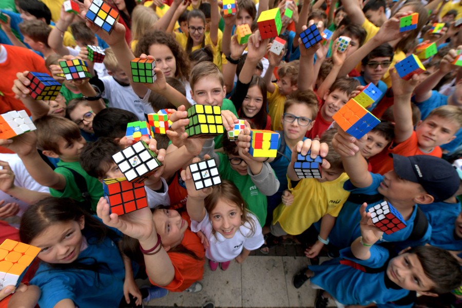 A group of schoolchildren hold up dozens of puzzle cubes.