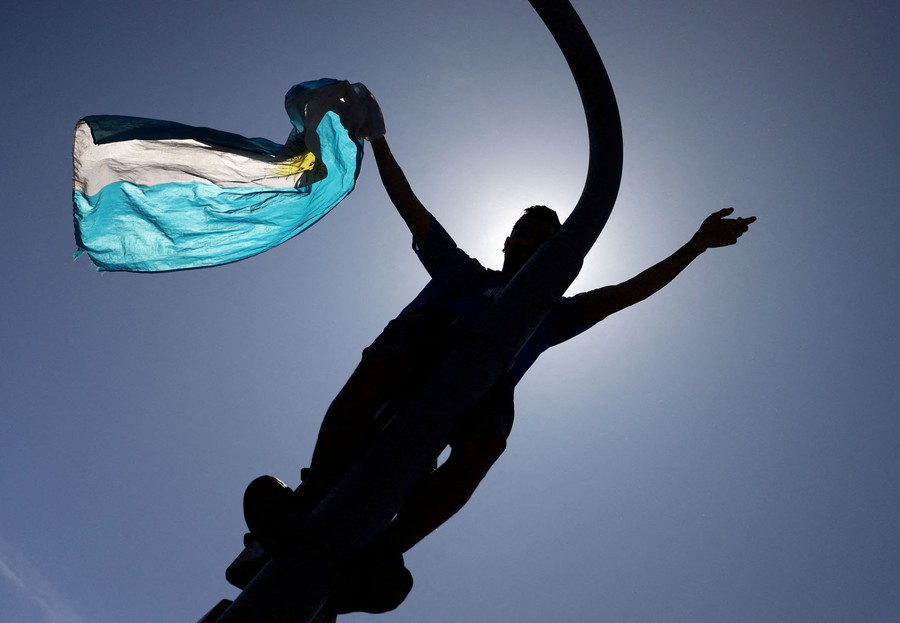 A fan waves the flag of Argentina while standing on top of a traffic light.