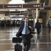 A man wearing a suit runs through the airport with his luggage