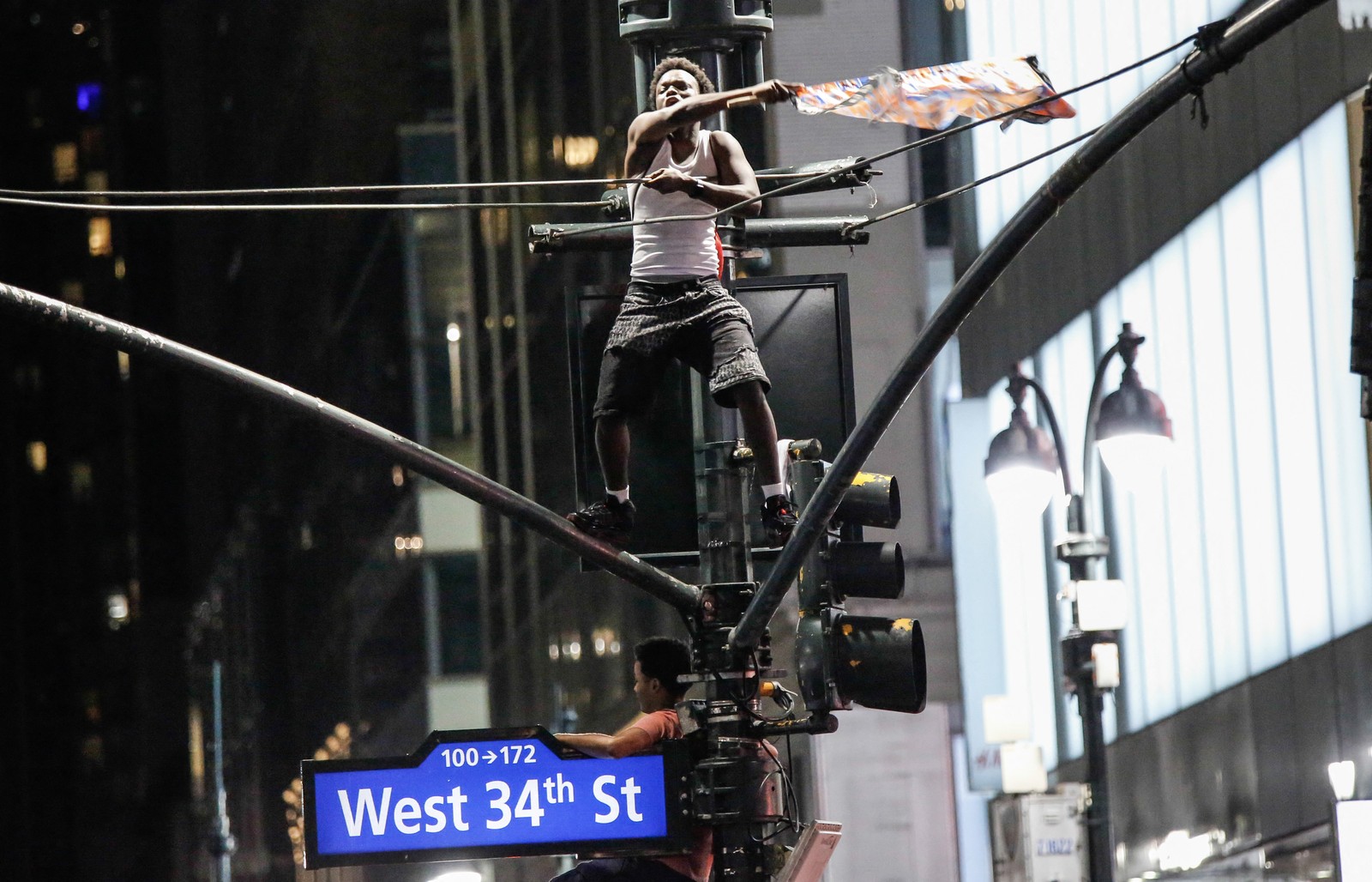 A Knicks fan waves a flag while standing on top of a traffic light pole.