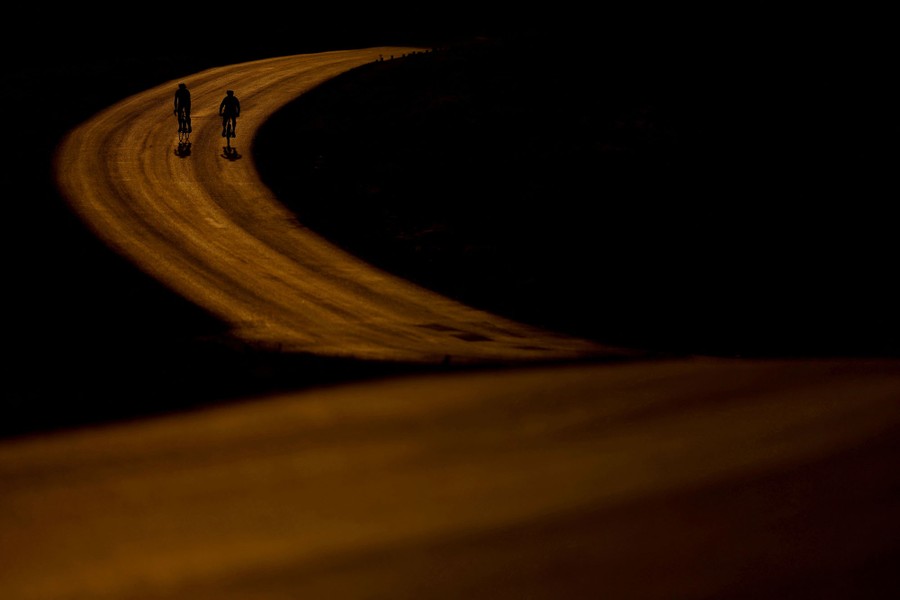 A sunrise view of two cyclists on a curving road.