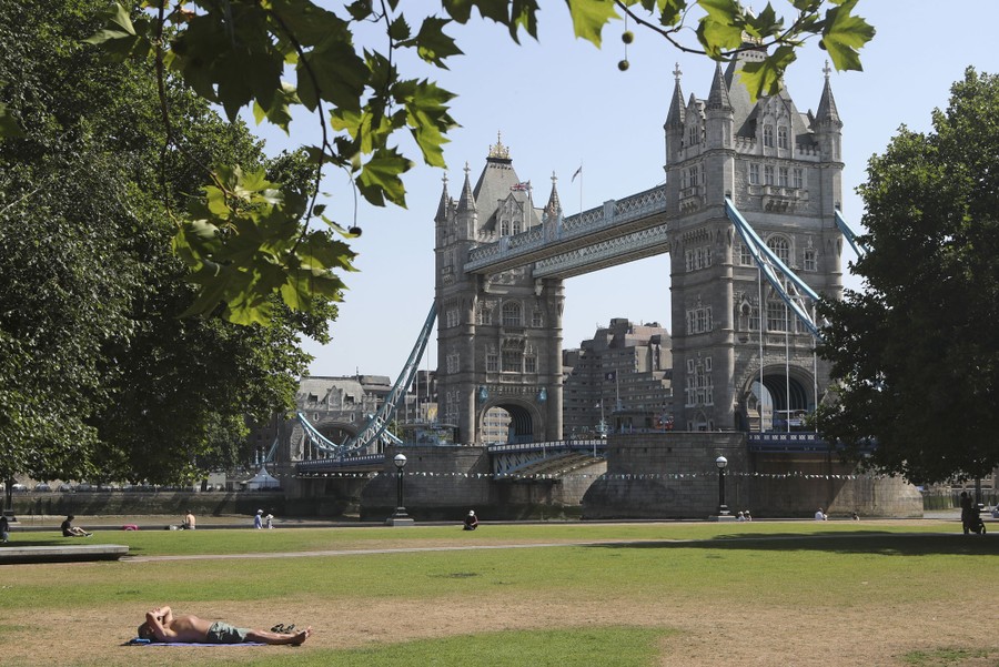 A man sunbathes on grass near the Tower Bridge in London.