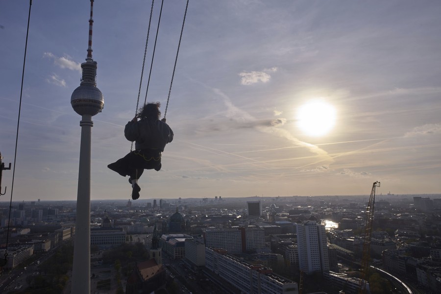 A woman swings on a swing suspended from a tall building overlooking many city buildings.