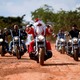 A man dressed as Santa Claus and several other men in regular clothes ride motorcycles on a dirt road.