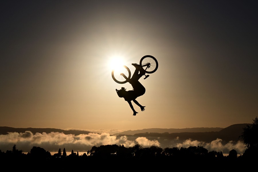 An athlete mid-jump on a bicycle, upside down, silhouetted against the sun
