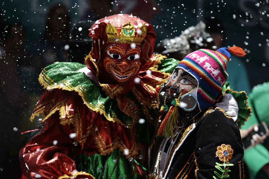 Two people in traditional costumes and masks hug during a festival.