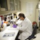 A man in a lab coat looks through the lens of a microscope
