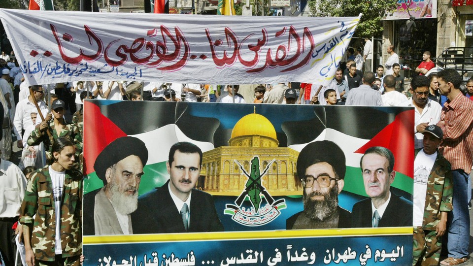 Protestors hold up a banner picturing late Ayatollah Ruhollah Khomeini, Syrian President Bashar al-Assad and Iranian Supreme Leader Ali Khameni and late Syrian Presidnet Hafez al-Assad.