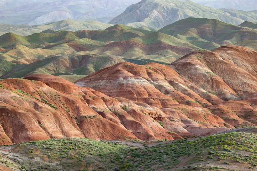 A view of distant hills, striped tan and white, and some covered with green foliage