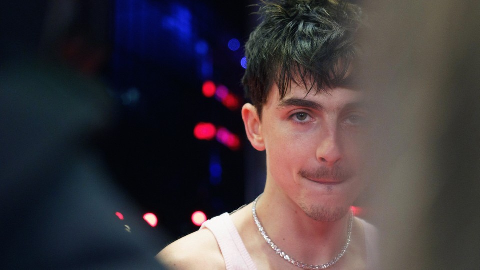 a photo of timothée chalamet; he is wearing a white tanktop and a silver chain necklace