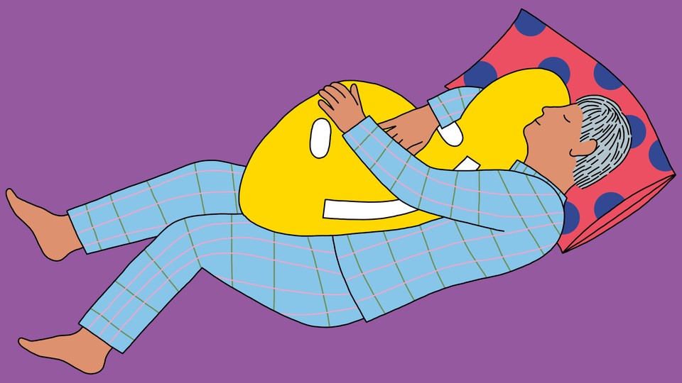 A person sleeping while hugging a pillow shaped like a smiley face