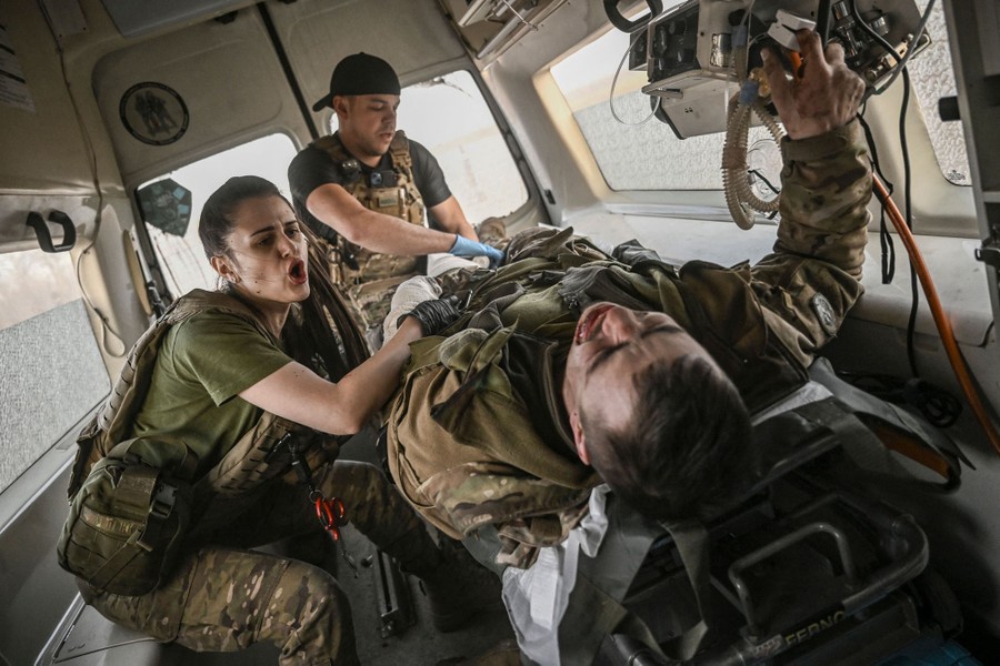 Two military paramedics ride in an ambulance beside a wounded serviceman.