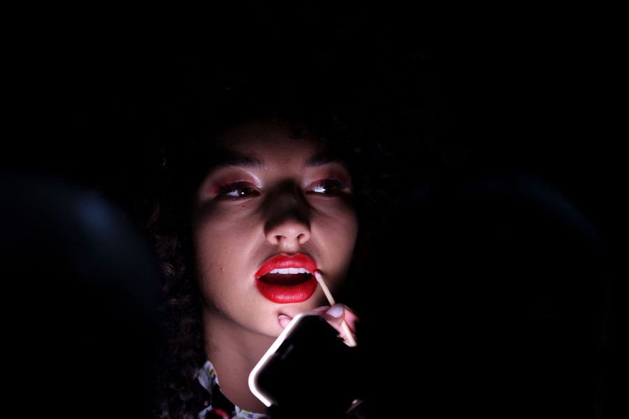 A model has makeup applied in a dark space with just her face illuminated.