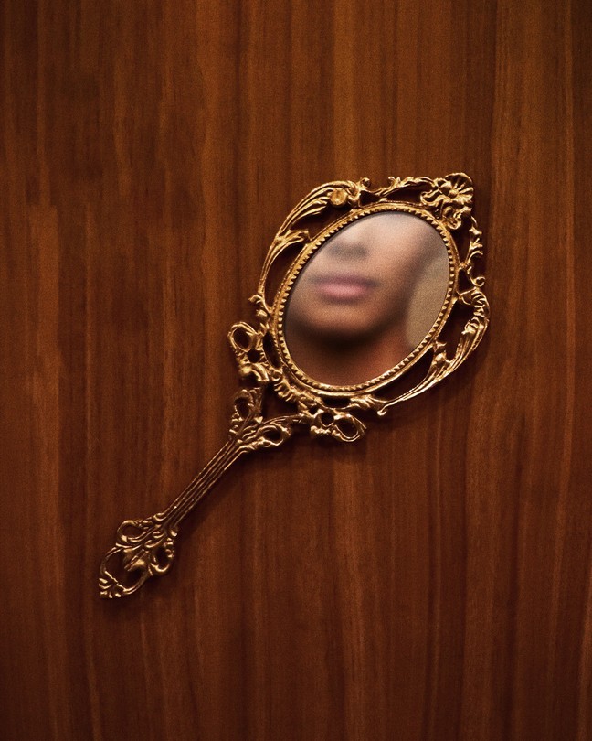 a fancy mirror on a wooden surface, the face of a black woman is reflected in the mirror