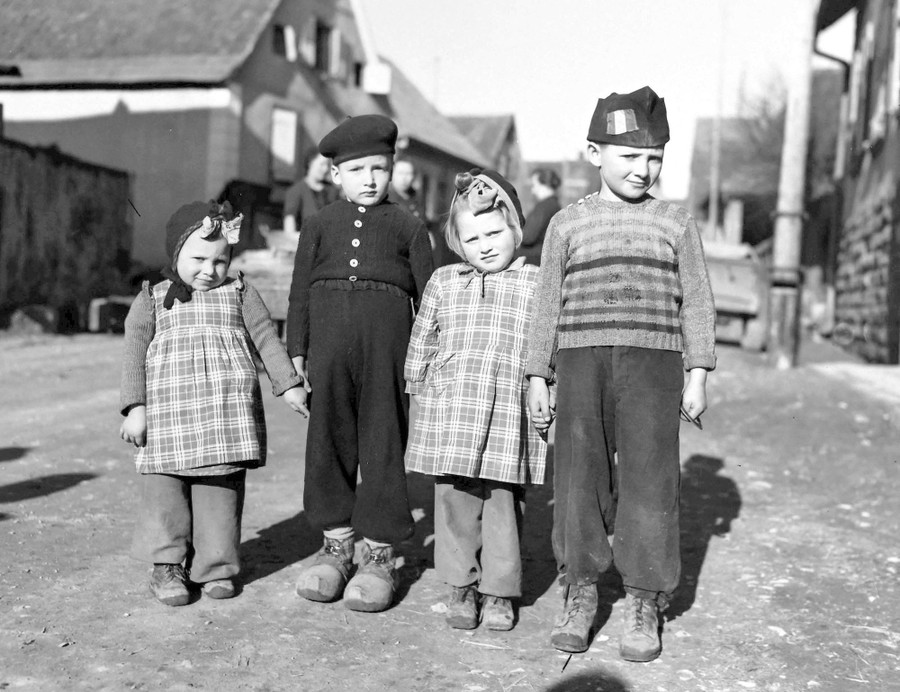Four young children hold hands while standing in a road, in 1945.
