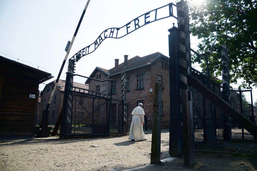 Pope Francis walks alone through a gate at Auschwitz.