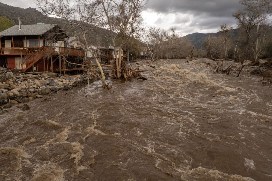 Flood-damaged homes line a rushing river.