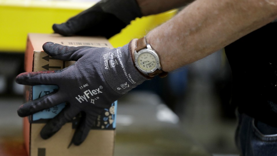 A person wearing a watch and gloves handles an Amazon package.