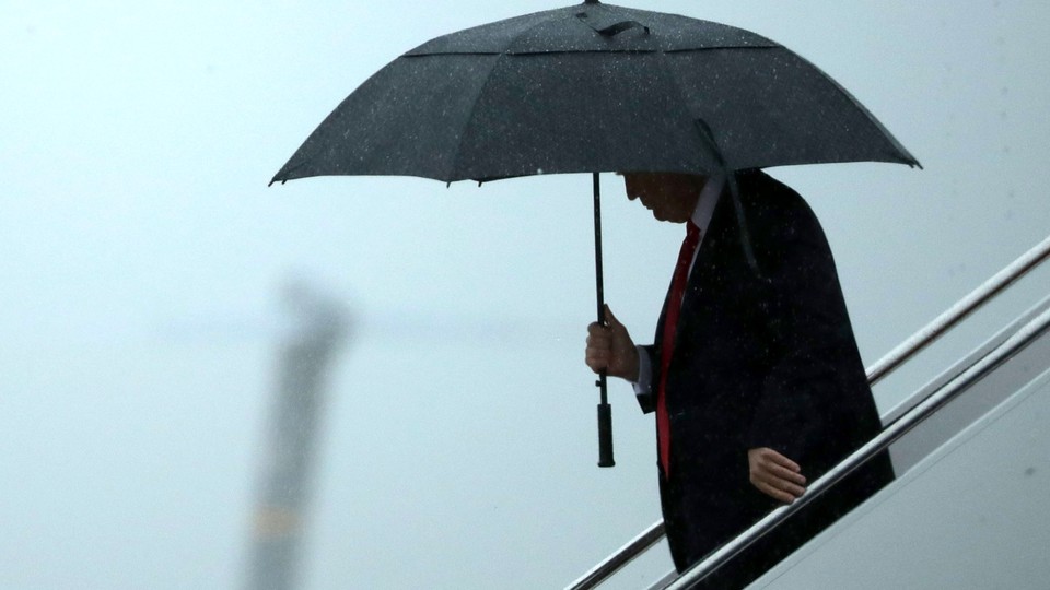 Donald Trump stands underneath an umbrella. 
