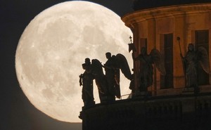 The full moon, behind statues of angels on a cathedral roof