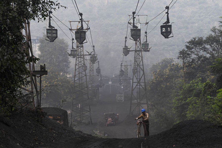 A worker pushes his bicycle on a dark road under a line of cable trolleys.