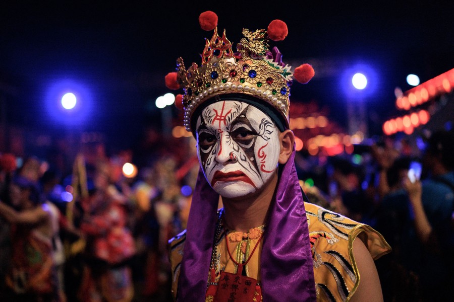 A festival-goer wears traditional face makeup and costume during a street performance.