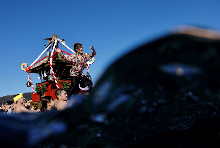A group of people carry a small shrine into the sea.