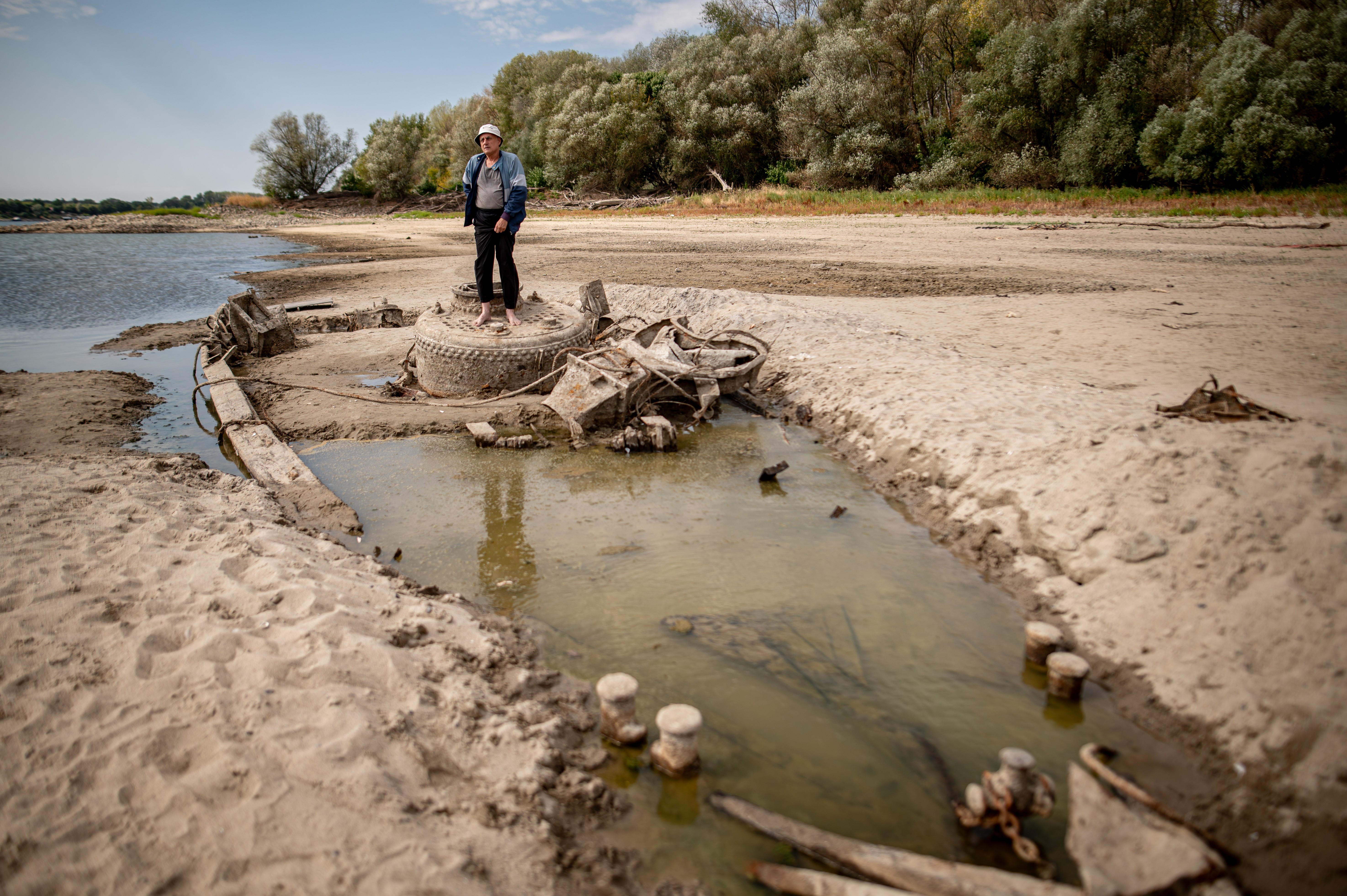 A man stands on the remains of an old World War II-era ship embedded in the exposed riverbed of the Danube.