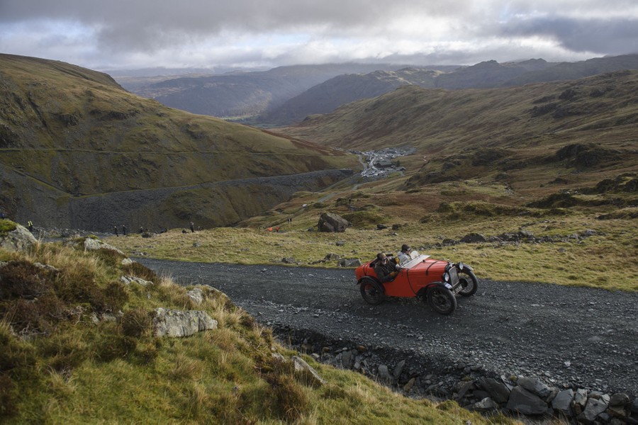 A vintage car is driven up a gravel mountain road.