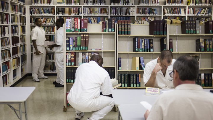 Men dressed in all white sit in a fluorescent room with bookshelves