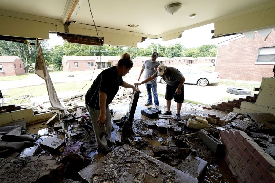 People stand in a heavily damaged room, picking over debris.