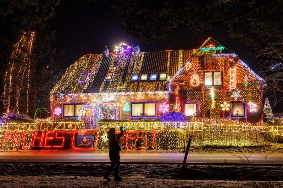 A woman takes a photo of a house illuminated with Christmas decorations.