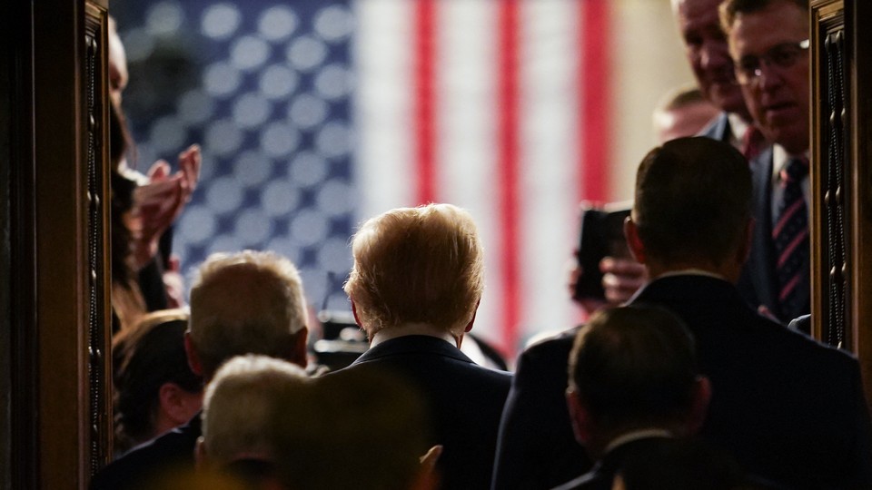 Donald Trump stands facing a U.S. flag that is blurred in the background.