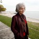 Alice Munro walks in front of a river and looks off to the right