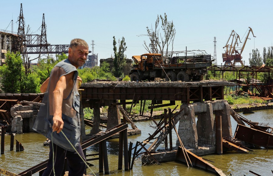A man stands on a bridge near a heavily damaged industrial area.