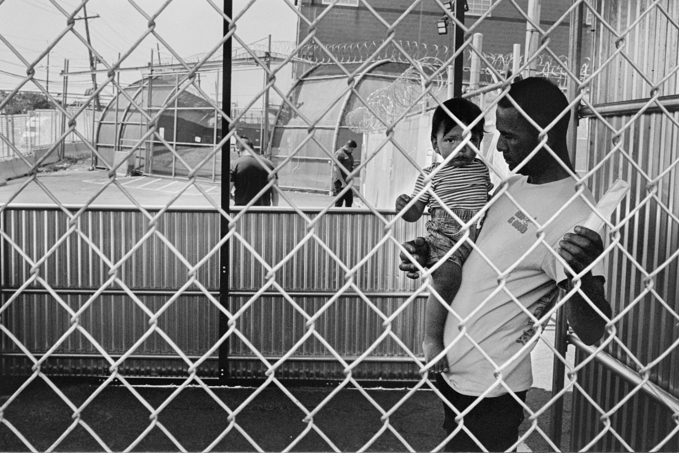 A man and a baby stand behind a fence