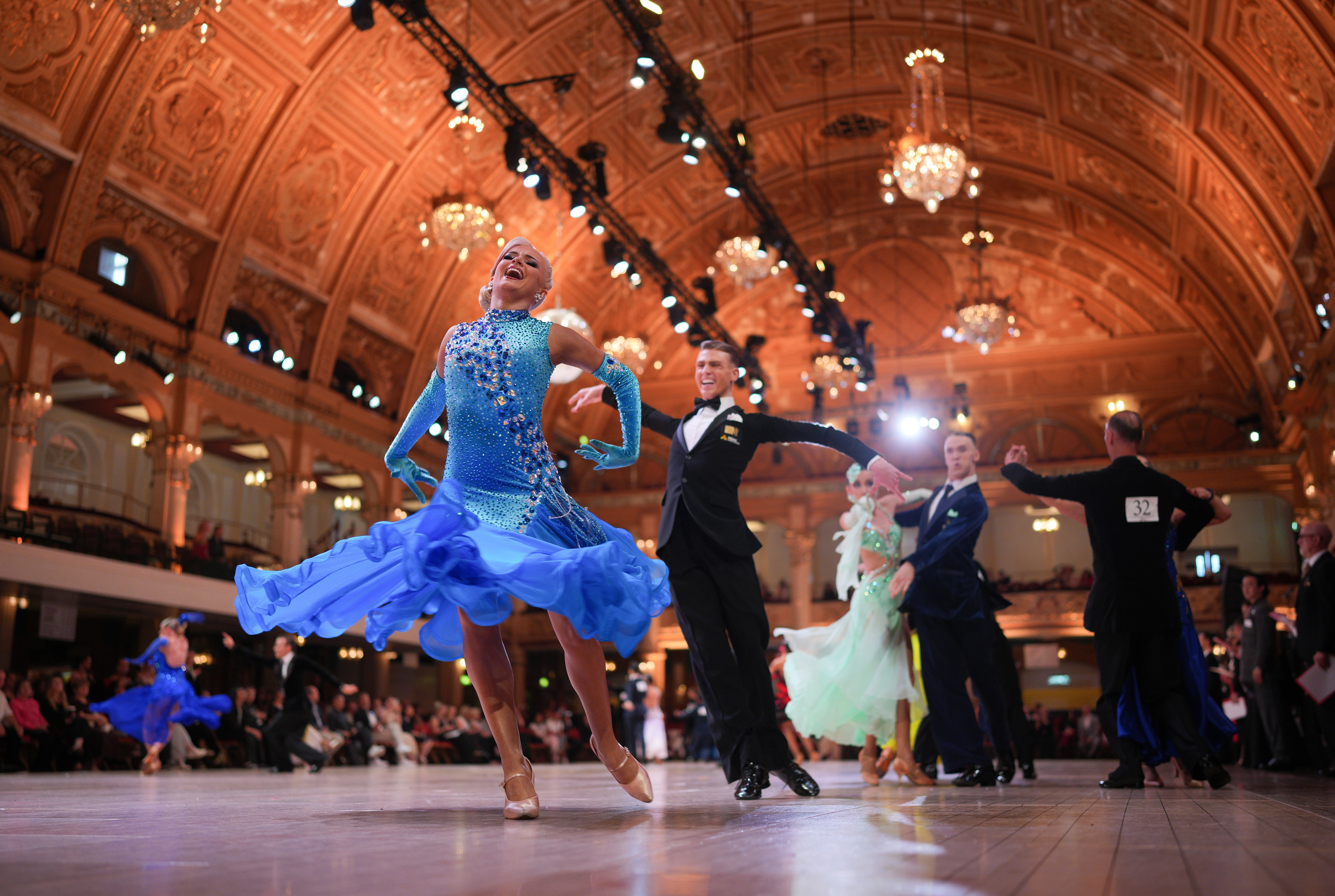 Ballroom dancers perform inside an ornate ballroom during a competition.