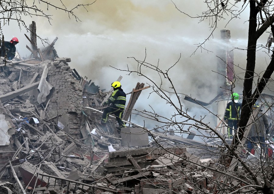 Several firefighters scaling piles of rubble and spraying water on smoking ruins.