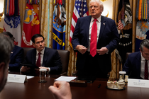 Color photograph of Donald Trump standing up behind a wooden table with Marco Rubio and Pete Hegseth on either side of him.