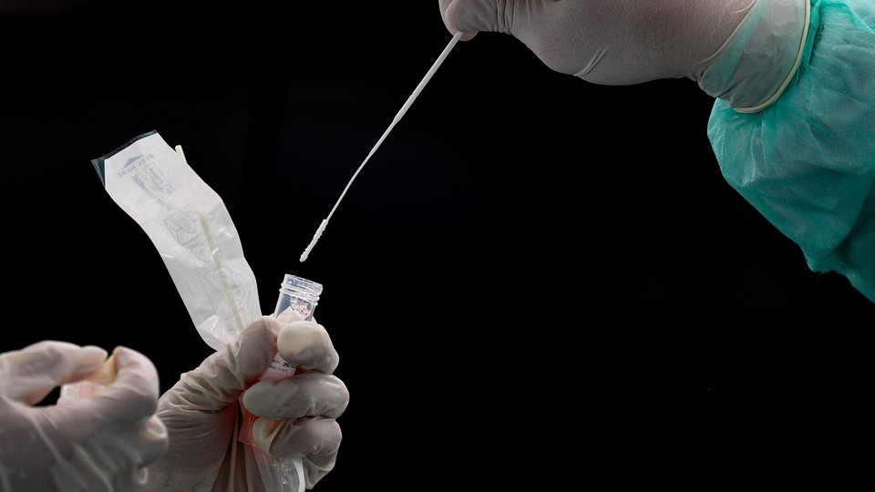 A gloved hand places a nasal swab in liquid to test for COVID-19