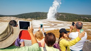photo of crowd of people holding up phones and tablets to take pictures of geyser spout