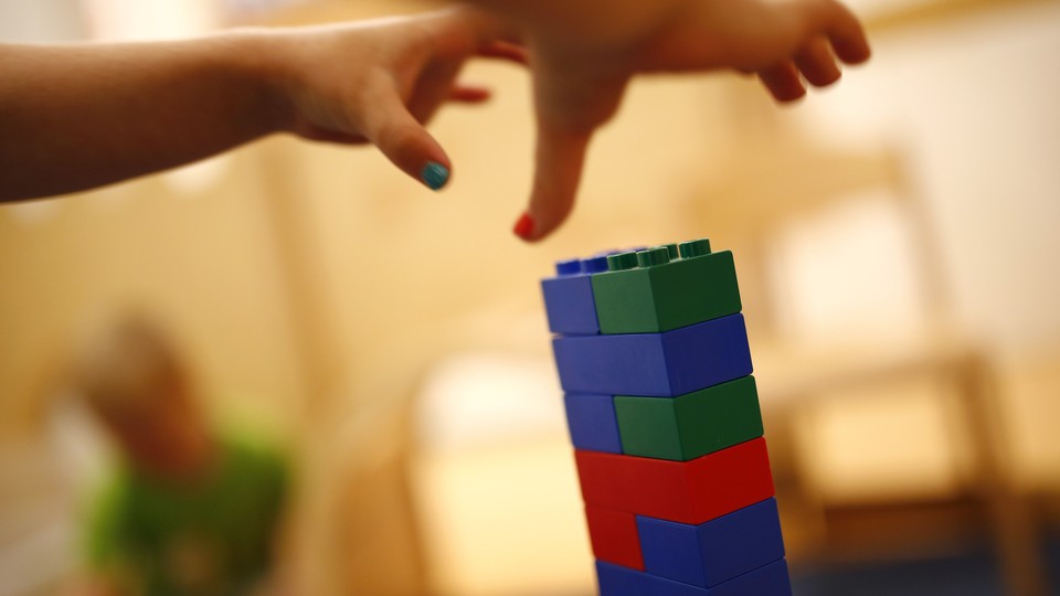 Two children's hands grab for a tower of LEGOs. 