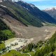 An aerial view of an Alpine valley after a massive landslide, with a cluster of houses being flooded on the uphill side.