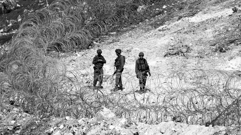 Black-and-white photo of three Israeli soldiers standing near circular barbed-wire fencing