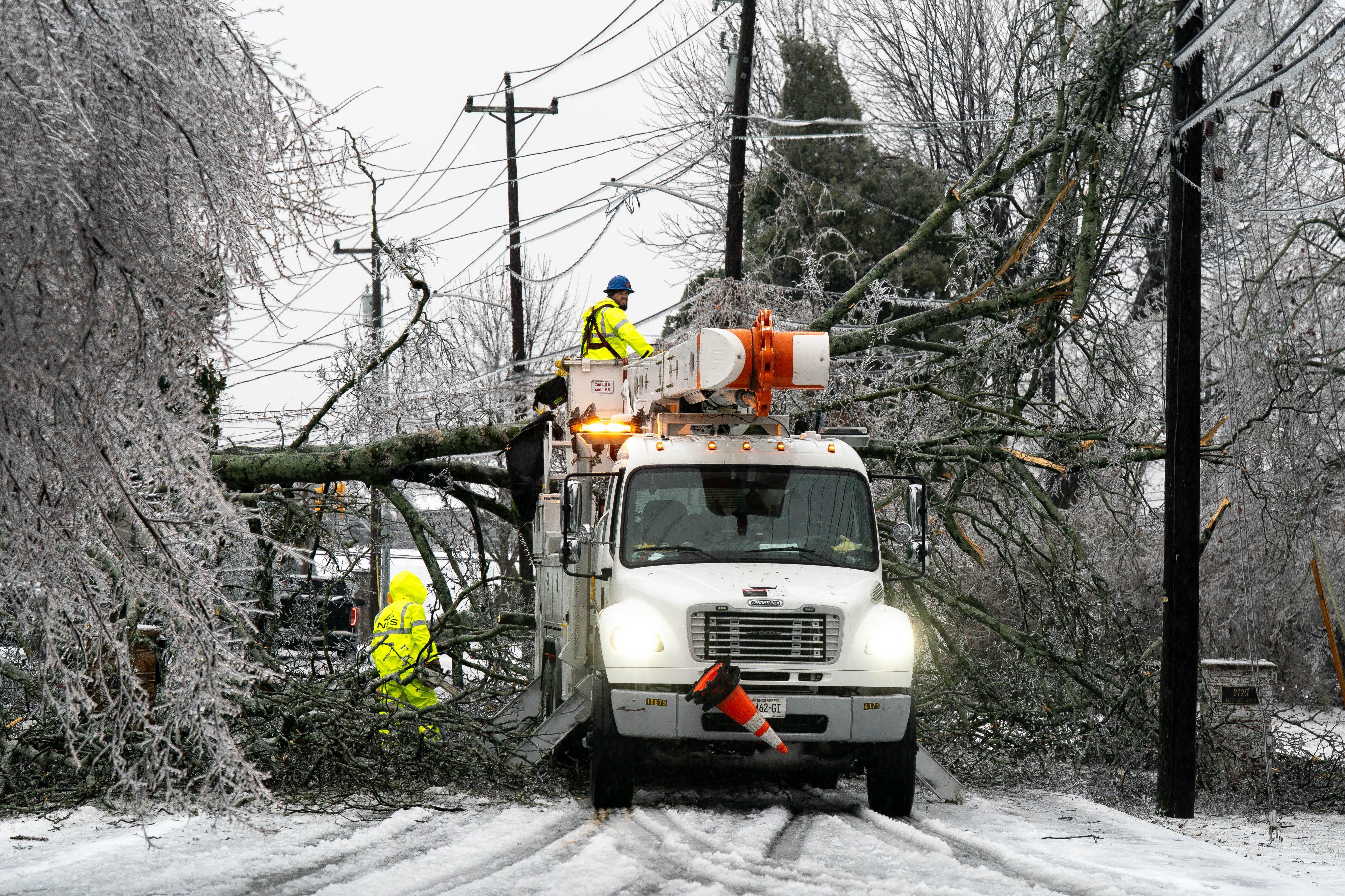 Workers try to restore power after a tree fell across powerlines during an ice storm.
